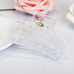 Close-up of clear acrylic hair claw clip with golden metal spring on white background