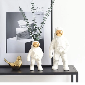 Modernas figuras de jarrón astronauta blancas y doradas con pájaro dorado en un escritorio