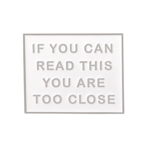 Macro detail of white enamel square badge with If You Can Read This text in grey