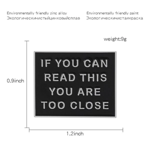 Macro view of black warning brooch with 'IF YOU CAN READ THIS YOU ARE TOO CLOSE' text
