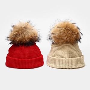 Close-up of red and beige knit hats with fluffy large fur pom-poms for winter warmth