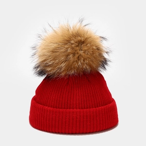 Detailed knit texture of a red winter hat featuring a fluffy faux fur pompom detail
