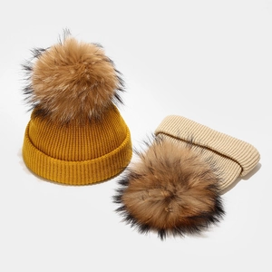 Knitted winter hat for babies with large fluffy fur pompom in yellow and beige colors