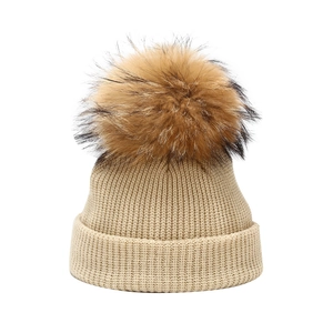 Knitted beige beanie for babies featuring a large fluffy fur pompom for winter warmth
