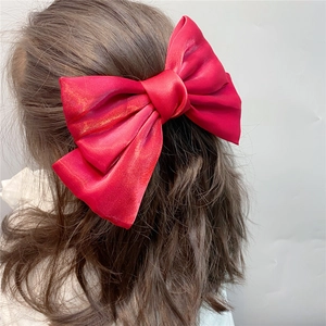 Elegant large red satin bow hair clip for women shown on a model with grey background