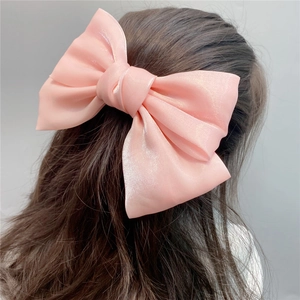 Rear view of a large pink satin bow hair clip on long hair with a silky texture finish