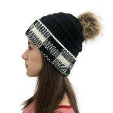 Detail of a black knit beanie with checkered cuff and a brown faux fur pom-pom topper