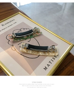 Detail of green marble and cream white shell acetate spring hair clips on a wooden surface