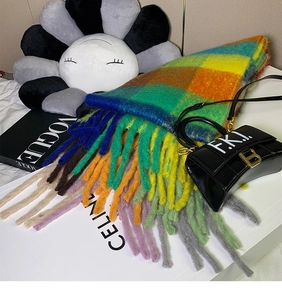 Detail of multi-color plaid scarf with long tassels draped over a white box and magazine