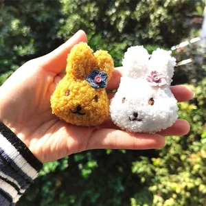 Handgefertigte Plüschhasen-Anhänger in Gelb und Weiß mit kleinen gestrickten Blumen