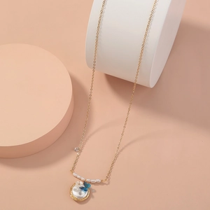 Minimalist gold necklace with blue butterfly floral pendant and pearl on pink podium