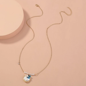 Elegant gold necklace with oval pendant featuring blue butterfly and pearls on pink stand
