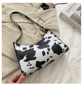 Detail of cow print shoulder bag with gold zipper on a beige blazer and magazine