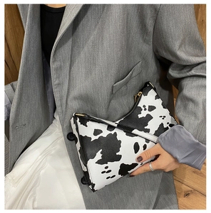 Close-up of stylish cow print shoulder bag with gold hardware and black zip closure