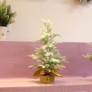 Miniature flocked Christmas tree with snow-dusted pine needles and burlap base on pink background