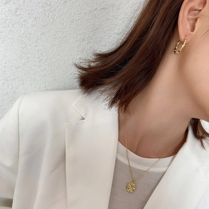 Close-up of gold twist hoop earrings and textured coin necklace on a female model