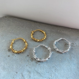 Detailed view of woven hoop earrings in gold and silver finish on a textured surface