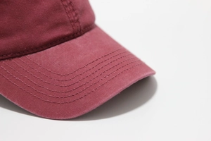 Close-up of precision stitching on a burgundy washed cotton baseball cap brim
