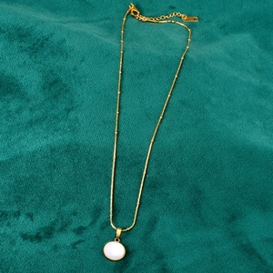 Detailed macro view of 18K gold bead chain with white shell pendant on green velvet