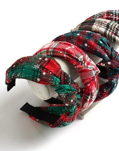 Close-up of five red and green plaid fabric headbands with snowflake patterns on a stand