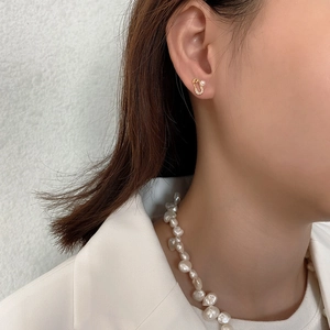 Detail of a golden safety pin pearl earring worn on the ear against a white background