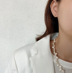 Close-up of gold hollow heart stud earrings and baroque pearl necklace on a model