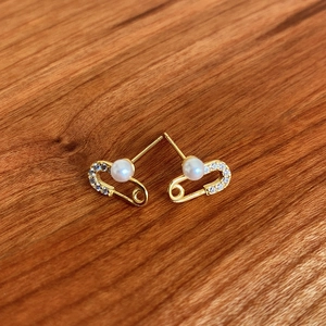 Detail of gold safety pin earrings with pearl and crystal on wood background