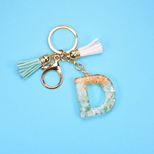 Detailed macro view of resin letter D keychain with gold foil, stones and mint tassels