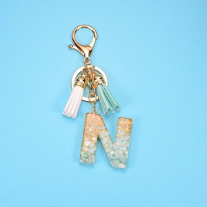 Letter N keychain with gold foil, mint stones, and colorful tassels on blue background