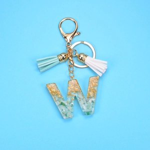 Detail of resin letter W keychain with gold foil flakes, green stones, and leather tassels