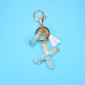Close-up of resin letter X keychain with gold foil, light blue stones and colorful tassels