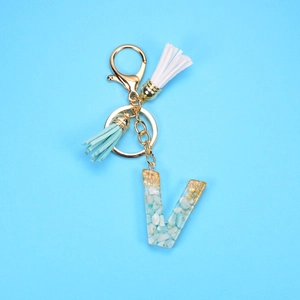 Detail view of resin letter V keychain with blue stones, gold foil, and colorful tassels