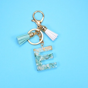 Detail showing letter E resin keychain with green stones, gold foil and tassels