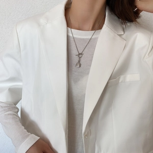 Detail of silver 925 coin pendant necklace with T-bar clasp worn with a white blazer