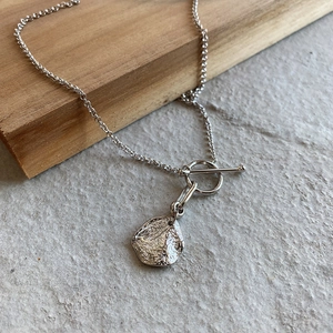Close-up of 925 silver necklace with textured round pendant and toggle clasp detail