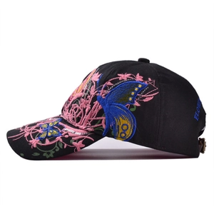 Dettaglio di farfalla blu e ricamo floreale rosa su un cappello di cotone nero