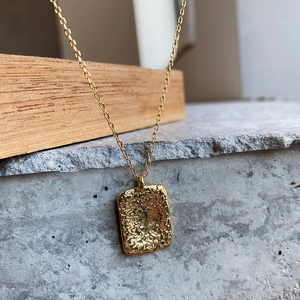 Close-up of golden rectangular pendant with artistic hammered texture on a fine chain