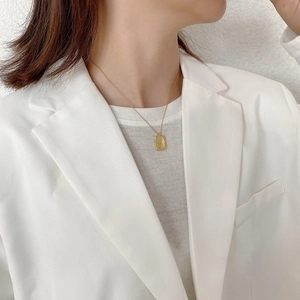 Close-up of a minimalist gold irregular square pendant necklace on a white blazer