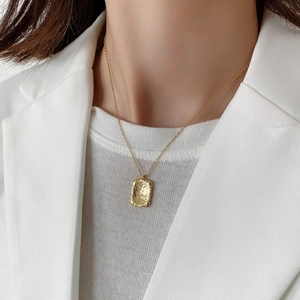 Detailed view of irregular hammered gold pendant necklace on a model wearing white