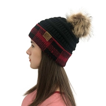Detail of red and black buffalo plaid knit beanie with a brown faux fur pom pom and C.C tag