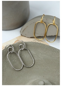 Close-up of gold and silver minimalist oval hoop earrings on textured concrete decor