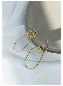 Detail of gold-plated geometric oval earrings on a stone tray with textured fabric
