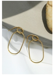 Detail of gold geometric hoop earrings on textured stone with elegant soft shadows