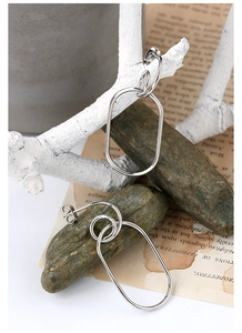 Macro detail of geometric silver layered oval hoop earrings on a decorative stone base