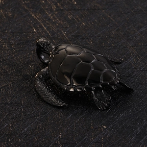 Macro detail of a black polished turtle pendant showing rich texture on a dark background