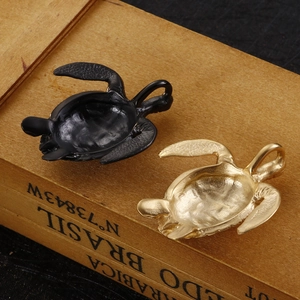 Close-up of turtle pendants in matte black and brushed gold finish on a vintage wood box