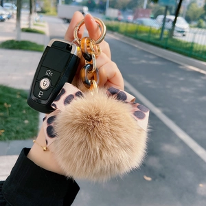 Detail of fox fur keychain with leopard print bow and amber chain link on hand