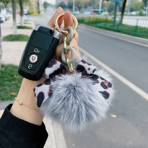 Detail view of fox fur keychain with grey plush ball and leopard print bow decoration