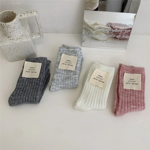 Detailed view of four pairs of thick wool socks in grey, white, and pink with tags