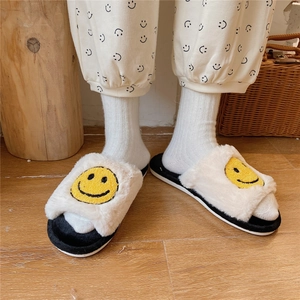 Close-up of cozy beige plush slippers with yellow smiley faces on wooden floor